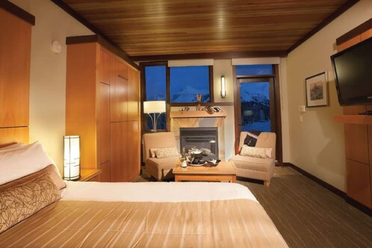 Una habitación de hotel con una cama, dos sillones, una mesa de centro, una chimenea y un televisor.