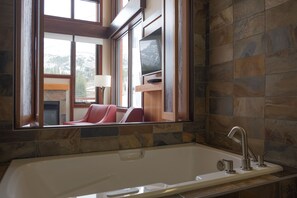 A modern bathroom with a large window, a bathtub, and a mirror reflecting the room.