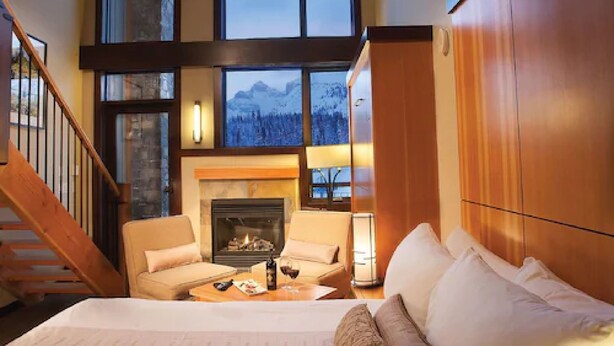 A spacious living room with a fireplace, a sofa, and a bed. A staircase is visible to the left. - Sunshine Mountain Lodge (Sunshine)