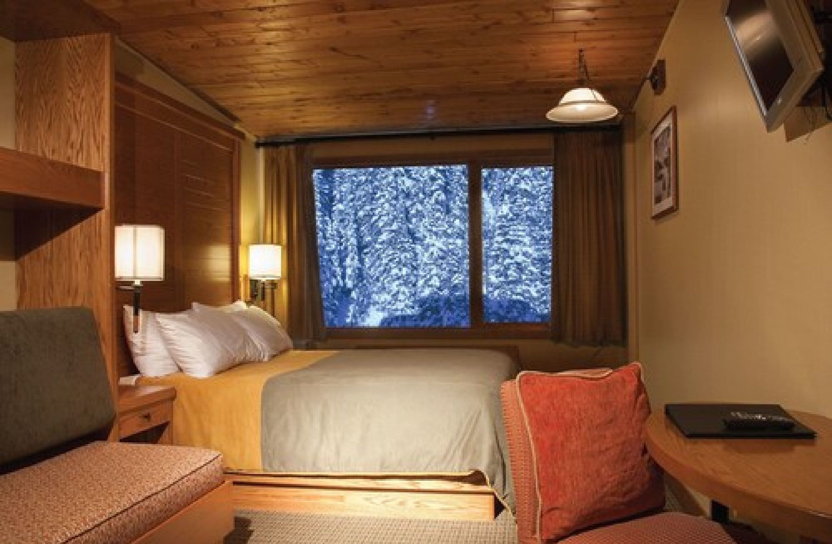Una habitación acogedora con una cama, un escritorio y una ventana con vistas nevadas.