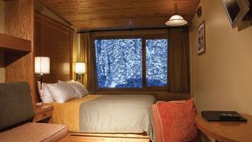 Una habitación acogedora con una cama, un escritorio y una ventana con vistas nevadas.