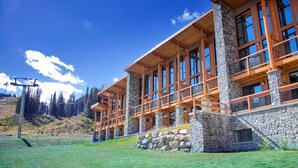 A multi-story building with wooden balconies and stone pillars, set against a mountainous backdrop. - Sunshine Mountain Lodge (Sunshine)
