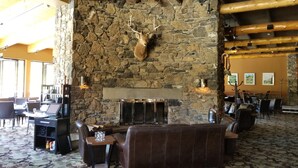 A stone fireplace with a mounted deer head, surrounded by leather seating and tables in a well-lit indoor space. - Sunshine Mountain Lodge (Sunshine)