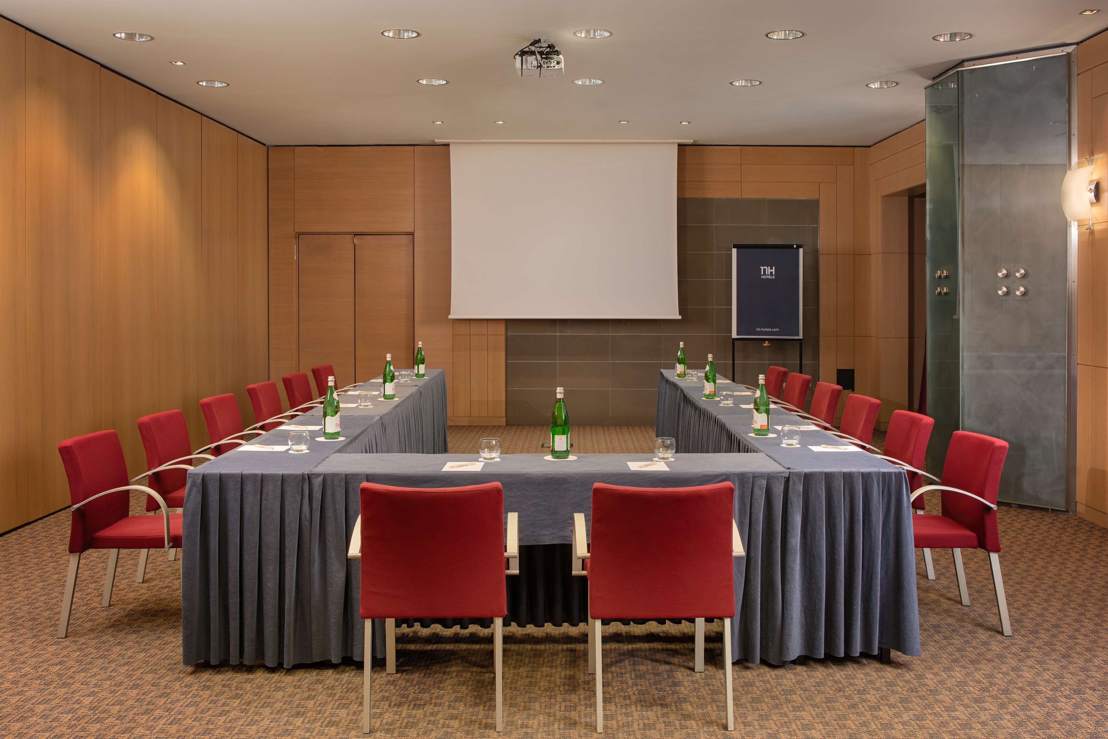 Une salle de conférence avec une longue table, des chaises rouges et un écran de projection.