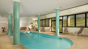 Uma piscina interior com design curvo, cercada por amplas janelas e colunas com mosaicos.