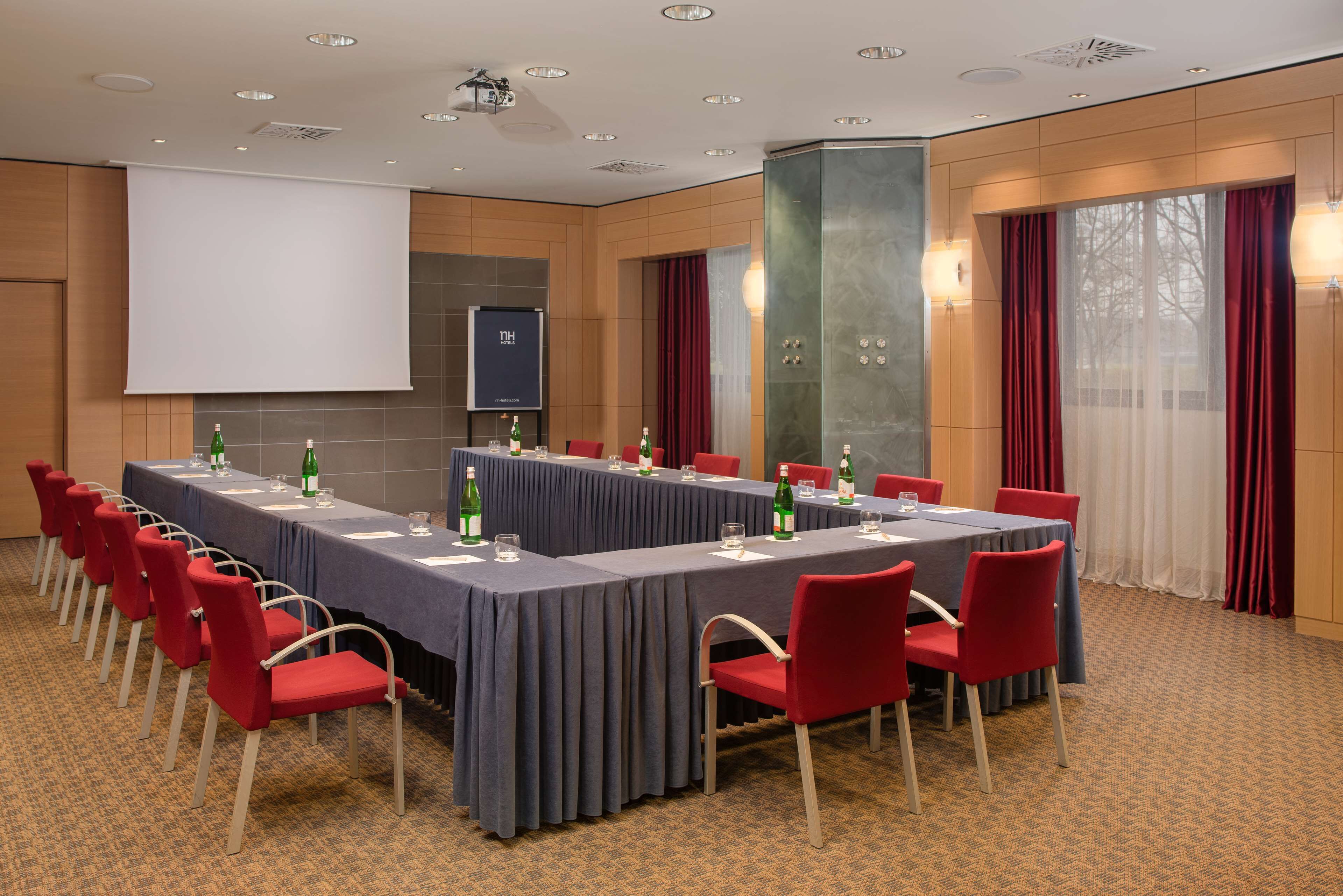 A conference room with a long table, red chairs, and a projector screen.