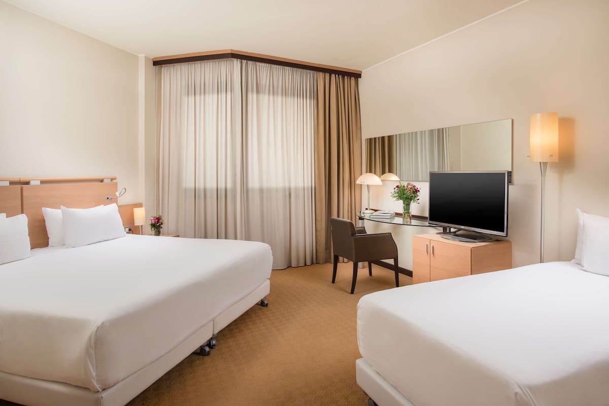A hotel room with two beds, a desk with a television, a mirror, and a lamp.