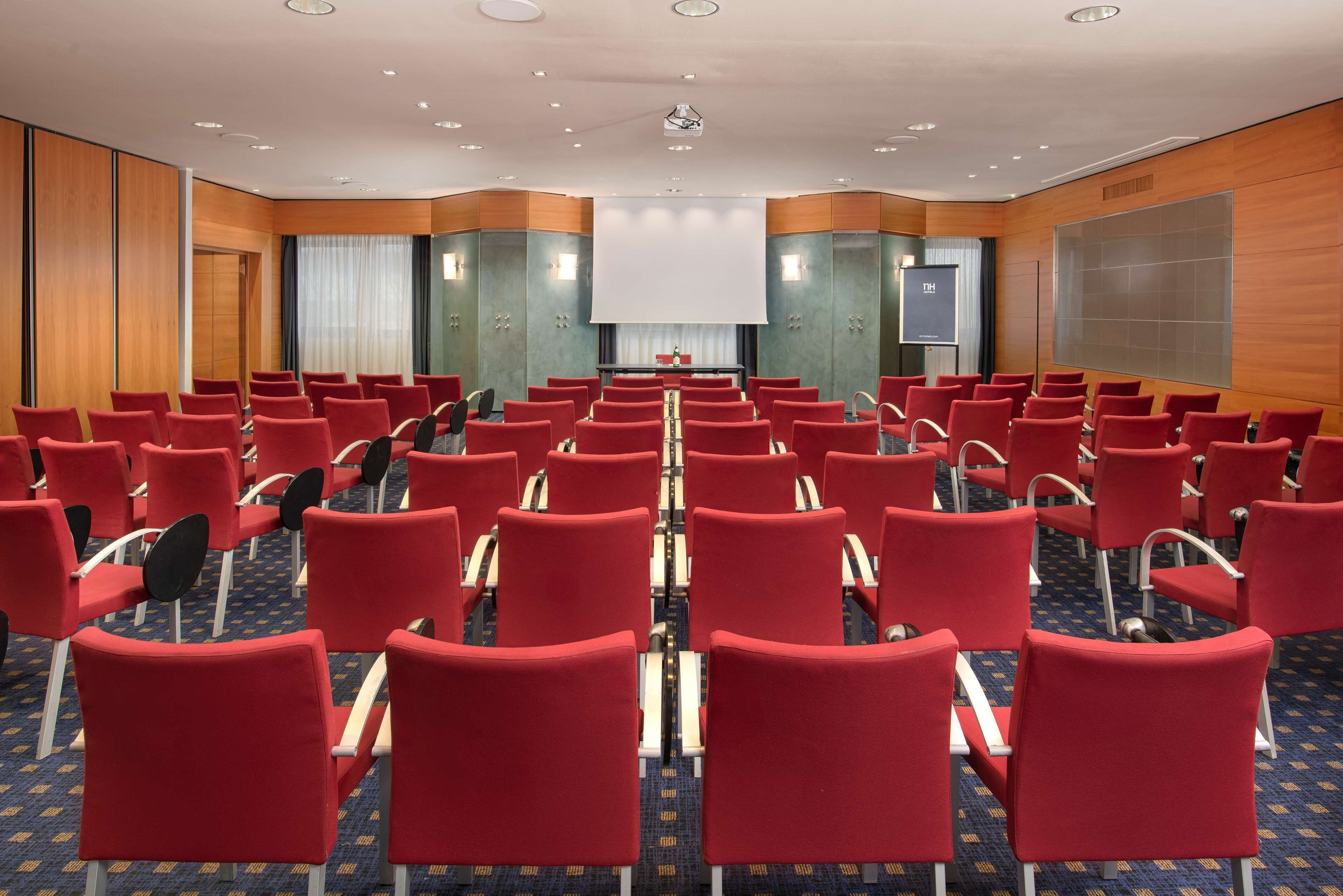 A conference room with rows of red chairs, a large screen at the front, and wooden paneling on the walls.