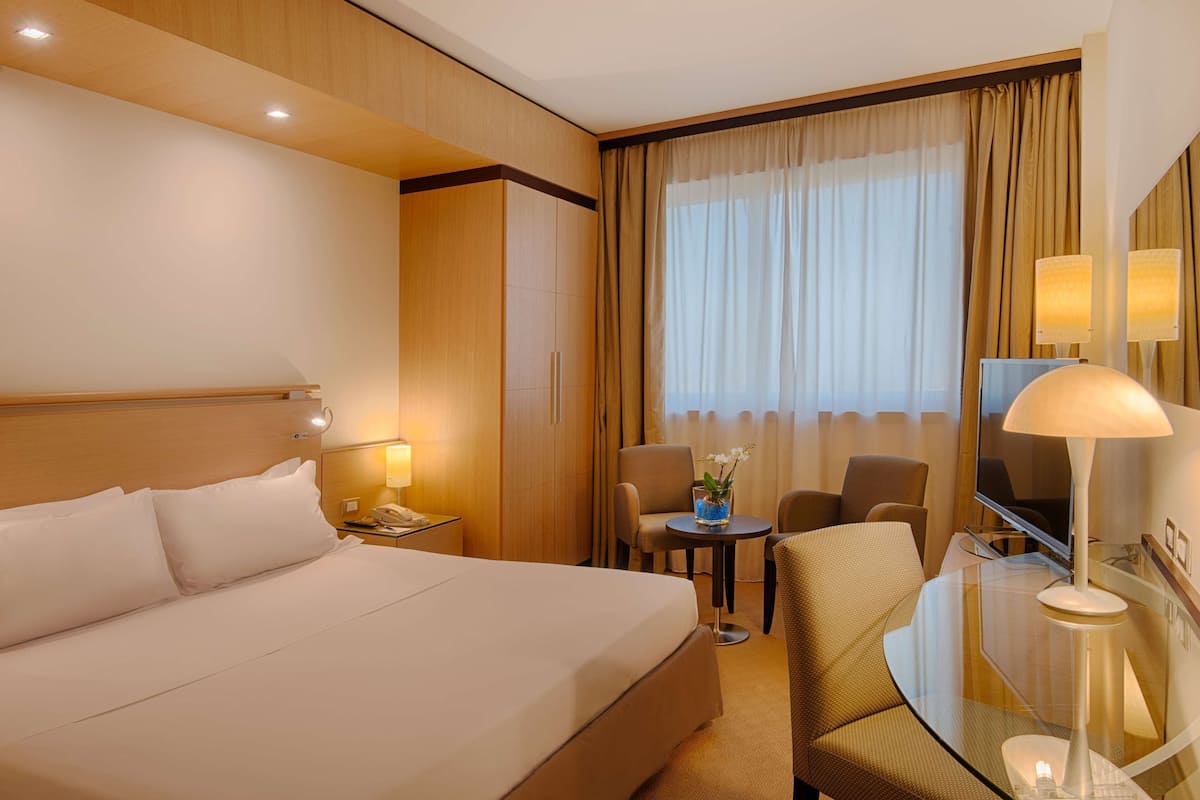 A hotel room with a bed, a desk, a chair, a TV, and a window with curtains.