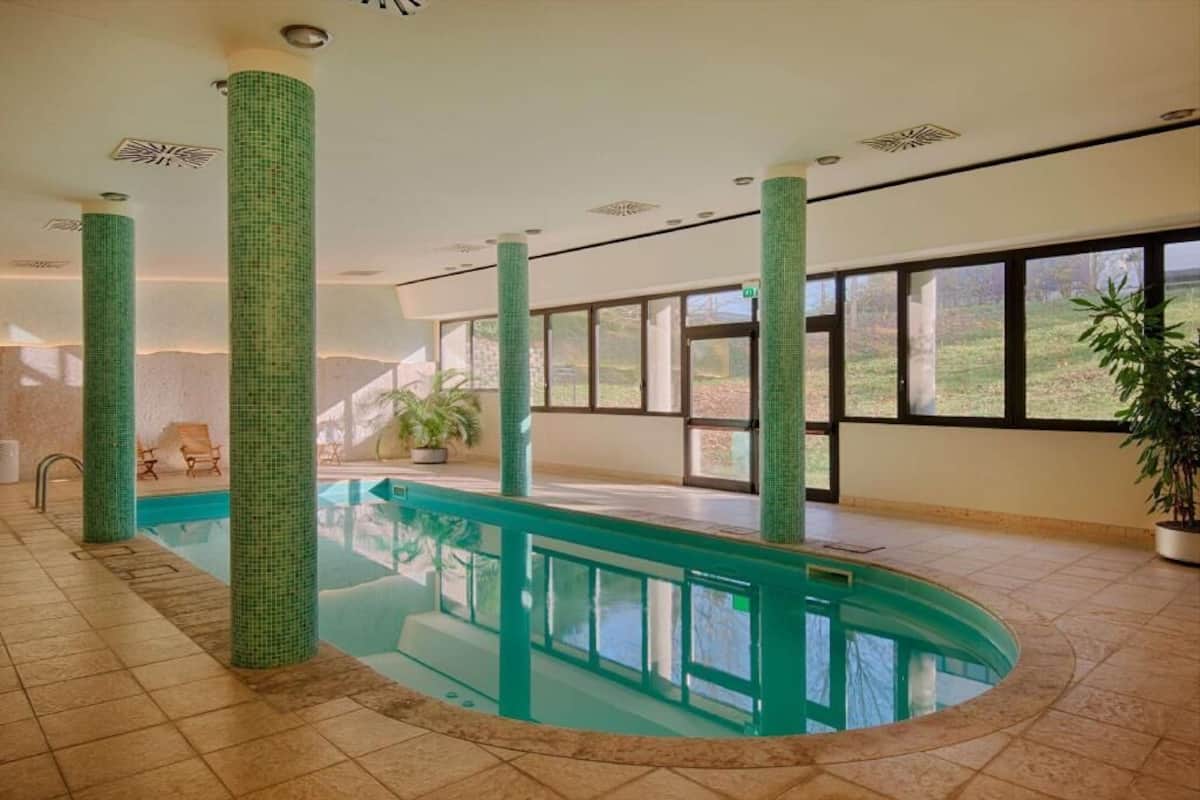 An indoor swimming pool with tiled walls, large windows, and a view of the outdoors.