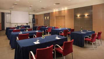 Un salón de conferencias con varias mesas y sillas, equipado con proyectores y pantallas.