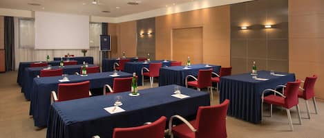 A conference room with multiple tables and chairs, equipped with projectors and screens.