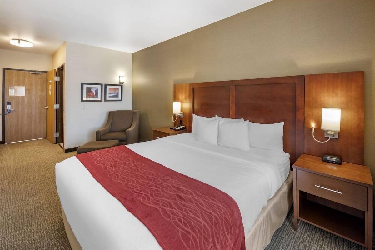 A hotel room with a large bed, two bedside tables with lamps, a chair, and a door.