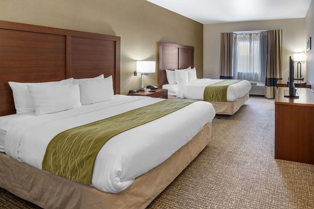 A hotel room with two beds, a desk, a chair, a lamp, and a TV.