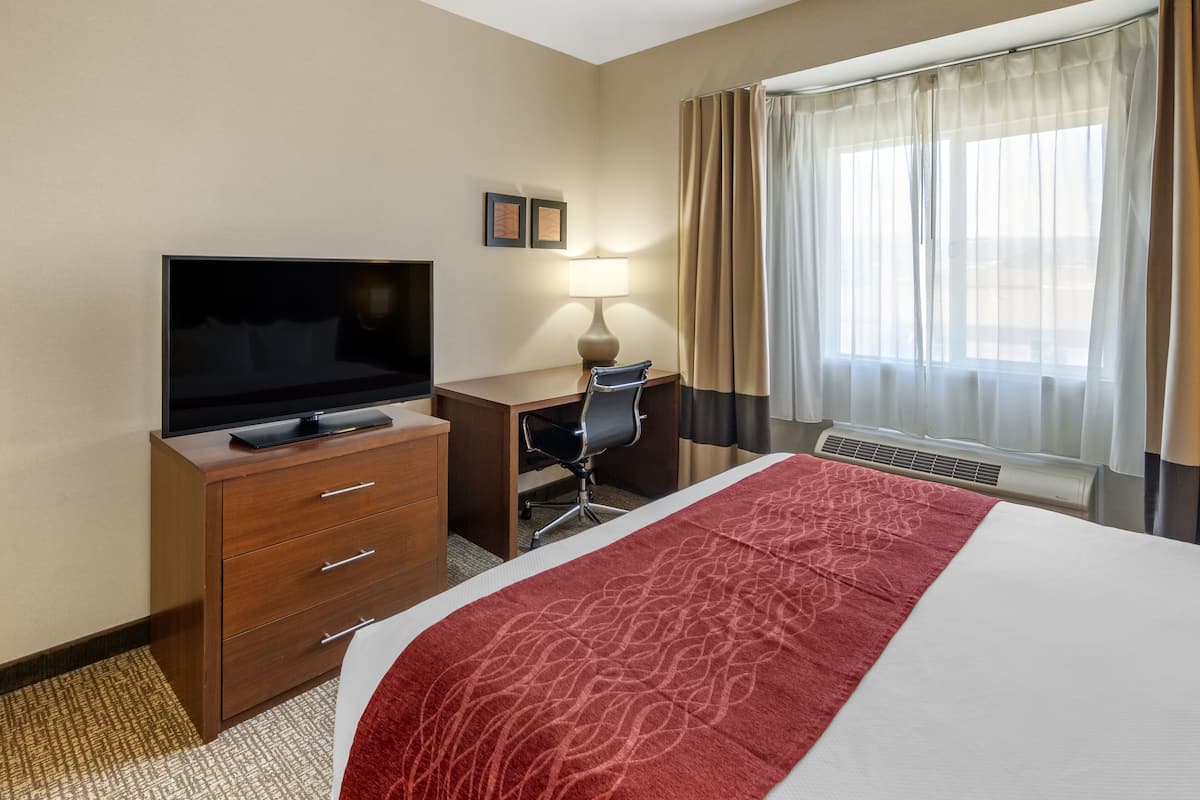 A hotel room with a bed, a desk with a chair, a television, a lamp, and a window with curtains.
