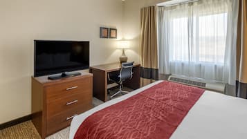 Une chambre d’hôtel comprenant un lit, un bureau avec une chaise, une télévision, une lampe et une fenêtre avec des rideaux.