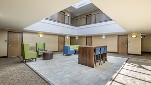 Un vaste espace intérieur doté d’un haut plafond, d’un espace de détente central avec des chaises et une table, et d’une mezzanine avec une rambarde.
