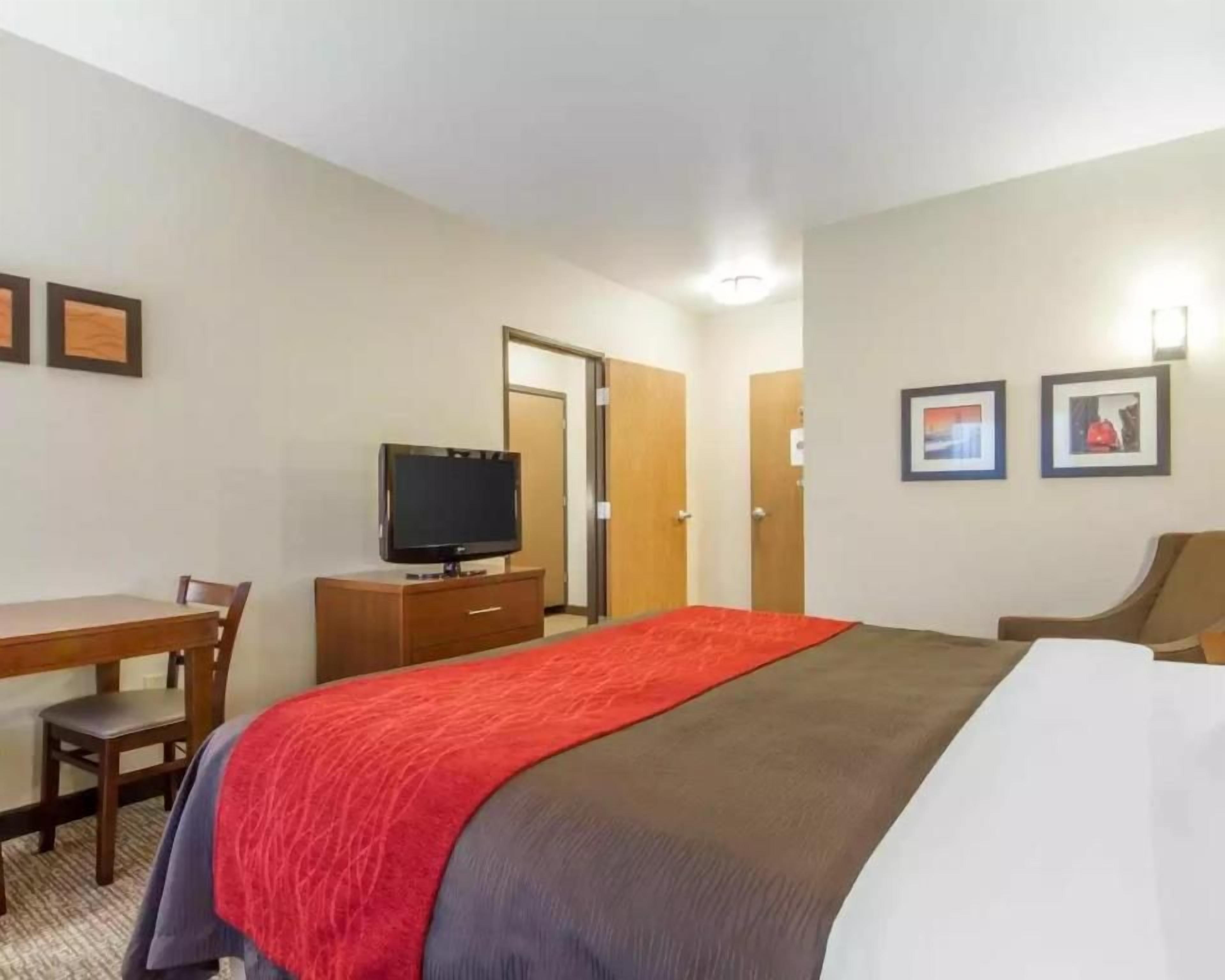 A hotel room with a bed, a desk with a chair, a television, and two framed pictures on the wall.