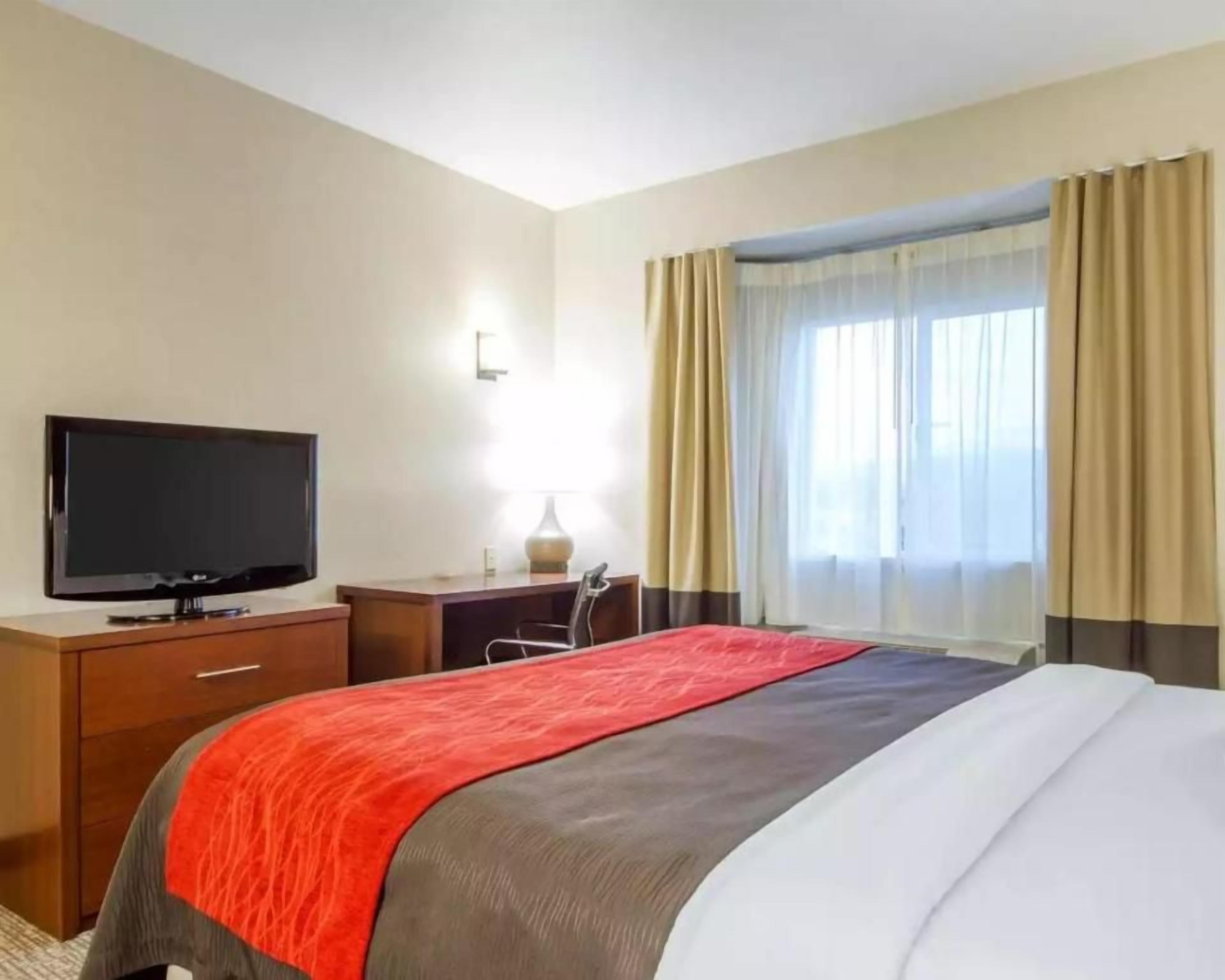 A hotel room with a bed, a television, a desk, and a window with curtains.