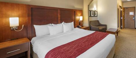 Une chambre d’hôtel avec un grand lit, une tête de lit en bois, un plaid rouge, une table de chevet avec une lampe et une chaise.