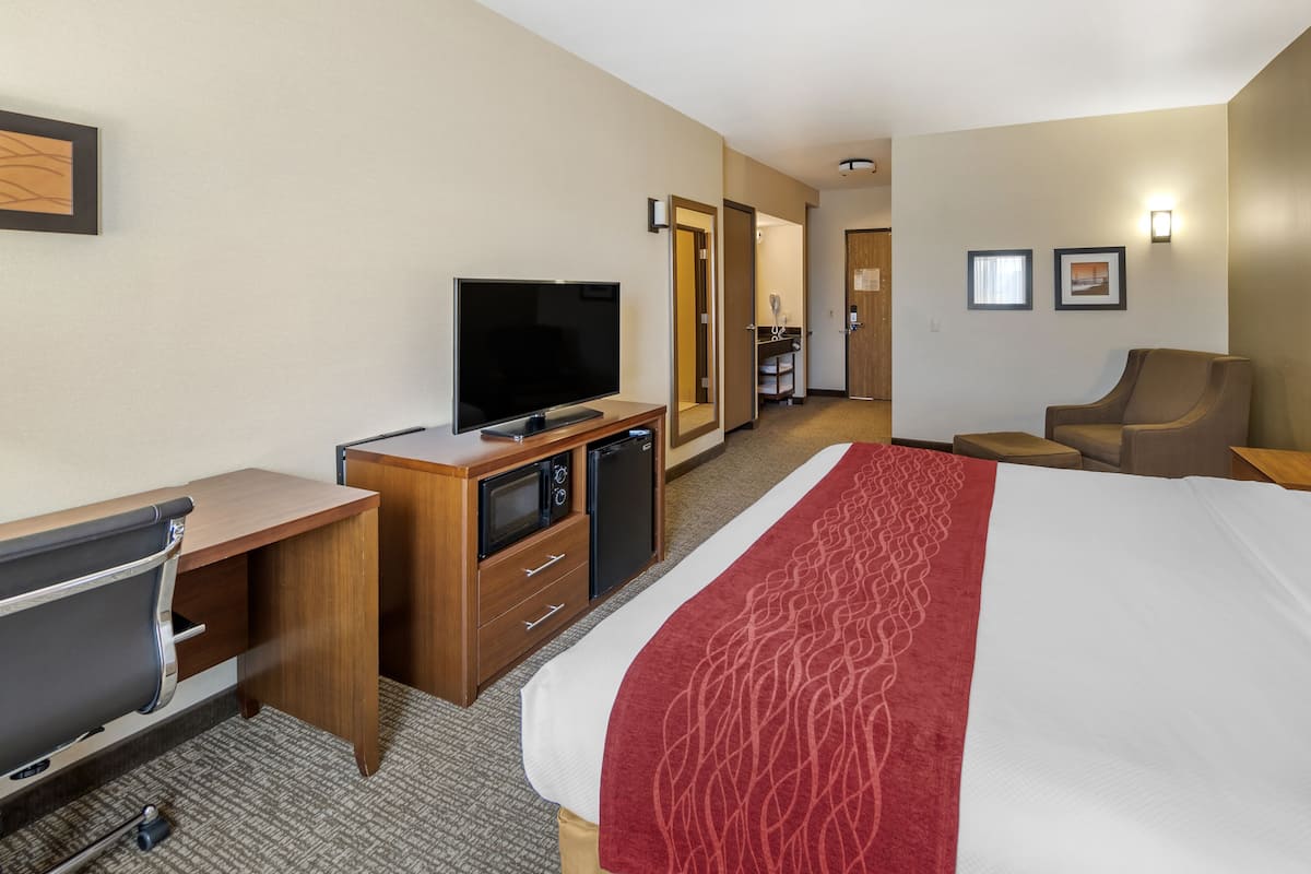 A hotel room with a bed, a desk with a television, a microwave, and a refrigerator.