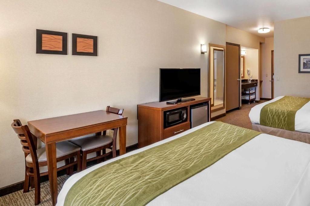 Una habitación de hotel con una cama, televisión, escritorio con sillas y microondas.