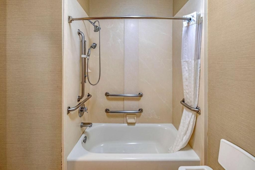 A bathroom with a bathtub, a shower with a grab bar, and a toilet.