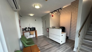 A compact living space with a kitchenette, a dining area with green chairs, a white dresser, and a staircase. - Mammas Inn (Niagara Falls)