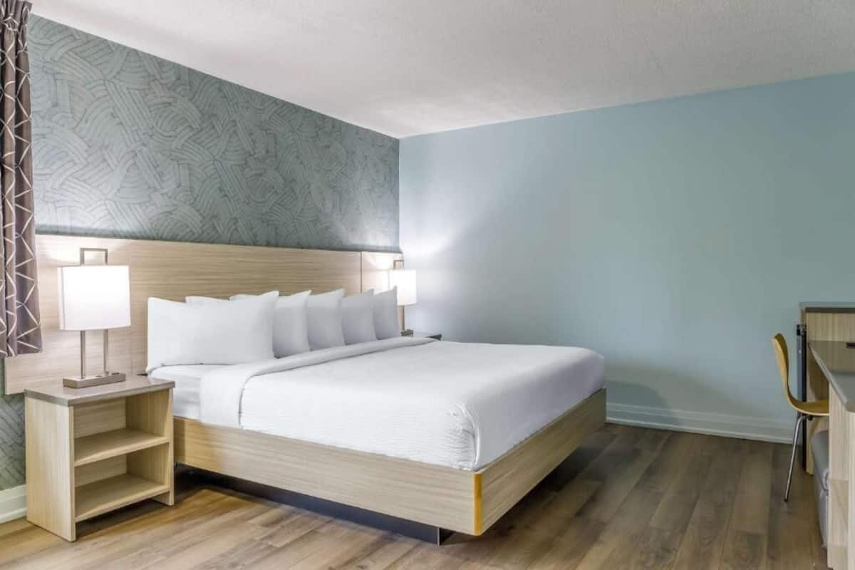 A neatly arranged hotel room with a bed, bedside tables, a chair, and a desk.