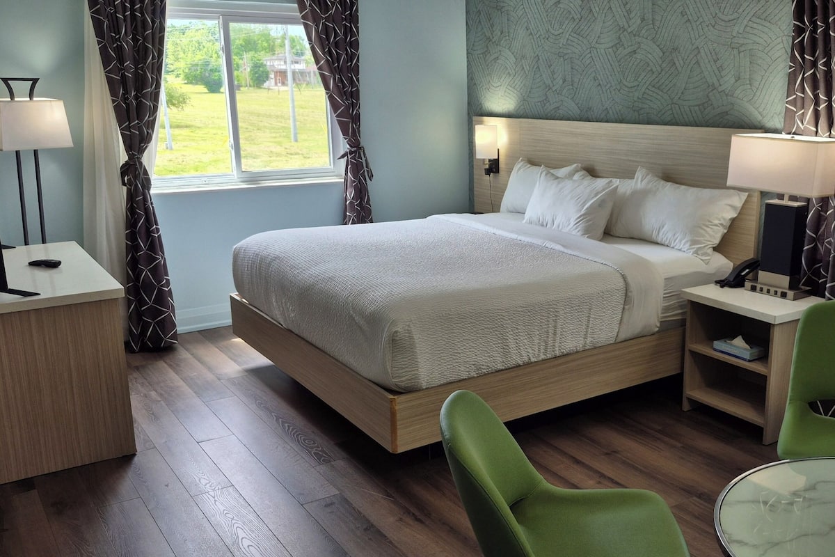 A hotel room with a bed, bedside lamps, a desk with a lamp, a chair, and a window with curtains.