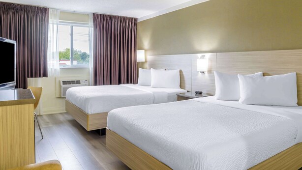 A hotel room with two beds, a desk, a chair, and a TV. - Mammas Inn (Niagara Falls)