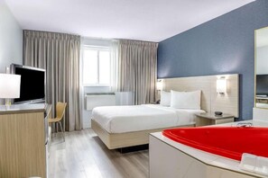 A hotel room with a bed, a TV, a desk, a chair, a red bathtub, and a window with curtains. - Mammas Inn (Niagara Falls)