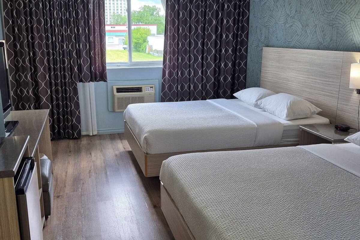 A hotel room with two beds, a desk with a computer, a TV, and a window with curtains.