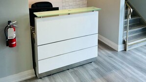 A reception desk with a white cabinet, a fire extinguisher on the wall, and a staircase to the right. - Mammas Inn (Niagara Falls)