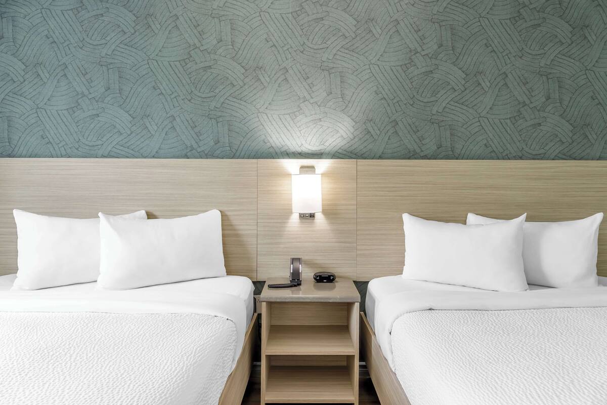 A hotel room with two beds, a nightstand, a wall-mounted lamp, and a patterned wall.