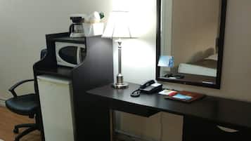 A hotel room with a bed, a desk with a computer, a microwave, a lamp, and a telephone.
