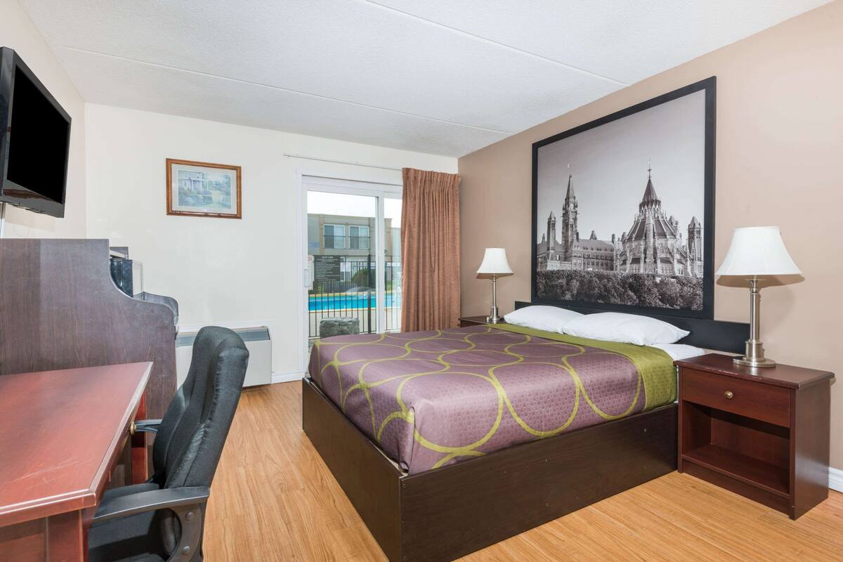Una habitación de hotel con cama, escritorio, silla y un cuadro grande en la pared.