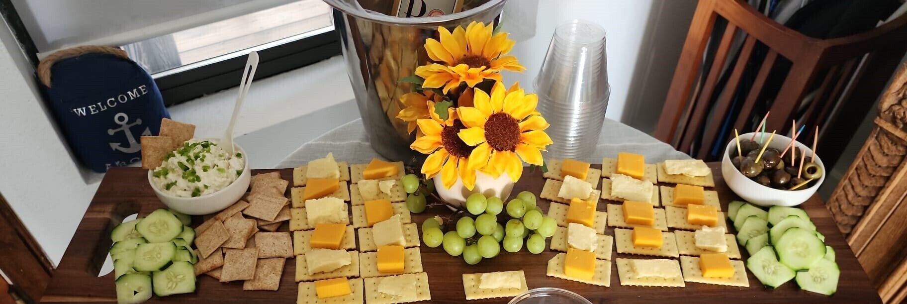 A table with cheese, crackers, grapes, and a sunflower centerpiece.
