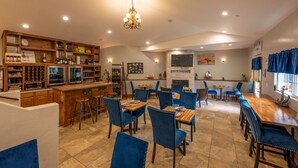 Un restaurant doté d’un bar, de chaises recouvertes de tissu bleu et de différentes bouteilles de vin exposées sur des étagères.