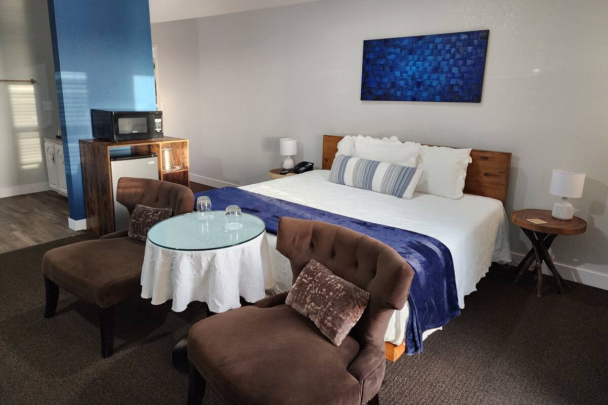 A hotel room with a bed, a small table with chairs, a microwave, a telephone, and a painting on the wall.