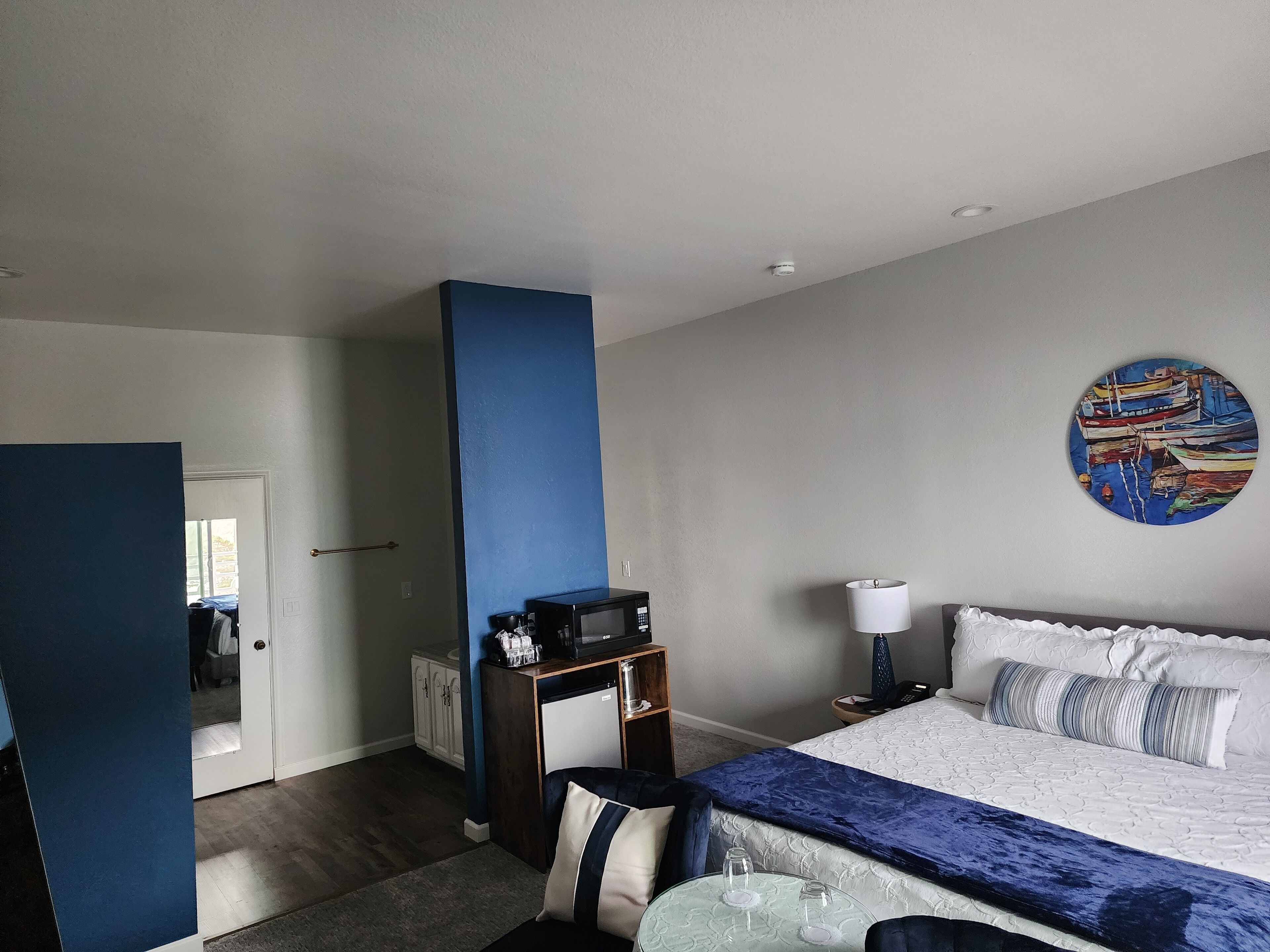 A hotel room with a bed, a desk, a chair, a lamp, and a painting on the wall.
