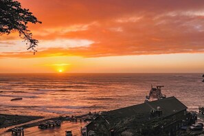 A sunset view over the ocean with a pier and a building with a sloped roof.