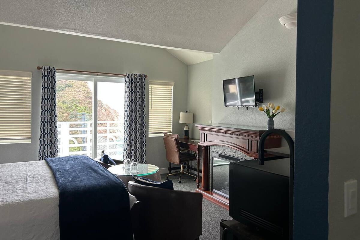 A hotel room with a bed, a desk with a chair, a TV, and a window with curtains.