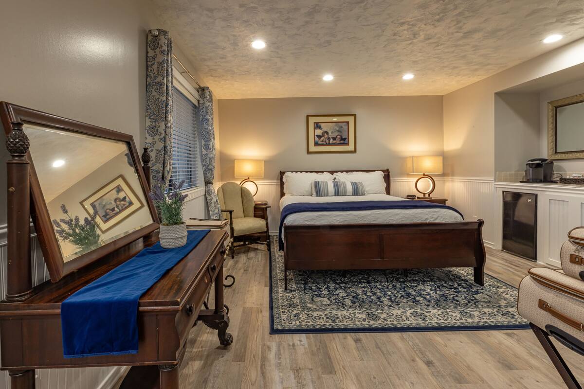 A bedroom with a wooden bed, a nightstand, a dresser, a mirror, and a large window with curtains.