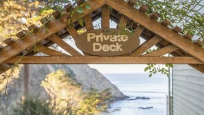 Une terrasse en bois, agrémentée d’une pancarte indiquant « Terrasse privée », qui mène à un sentier bordé de rampes et offrant une vue sur l’océan.