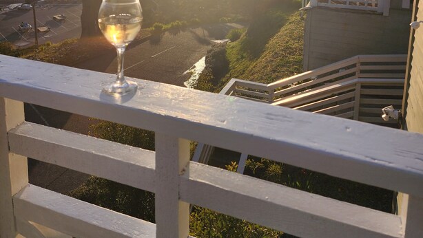 Un balcon avec un verre de vin, offrant une vue sur la côte, avec des arbres et un bâtiment doté d’une véranda.