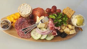 Una tabla de fiambres con diversos quesos, carnes, frutas y galletas.