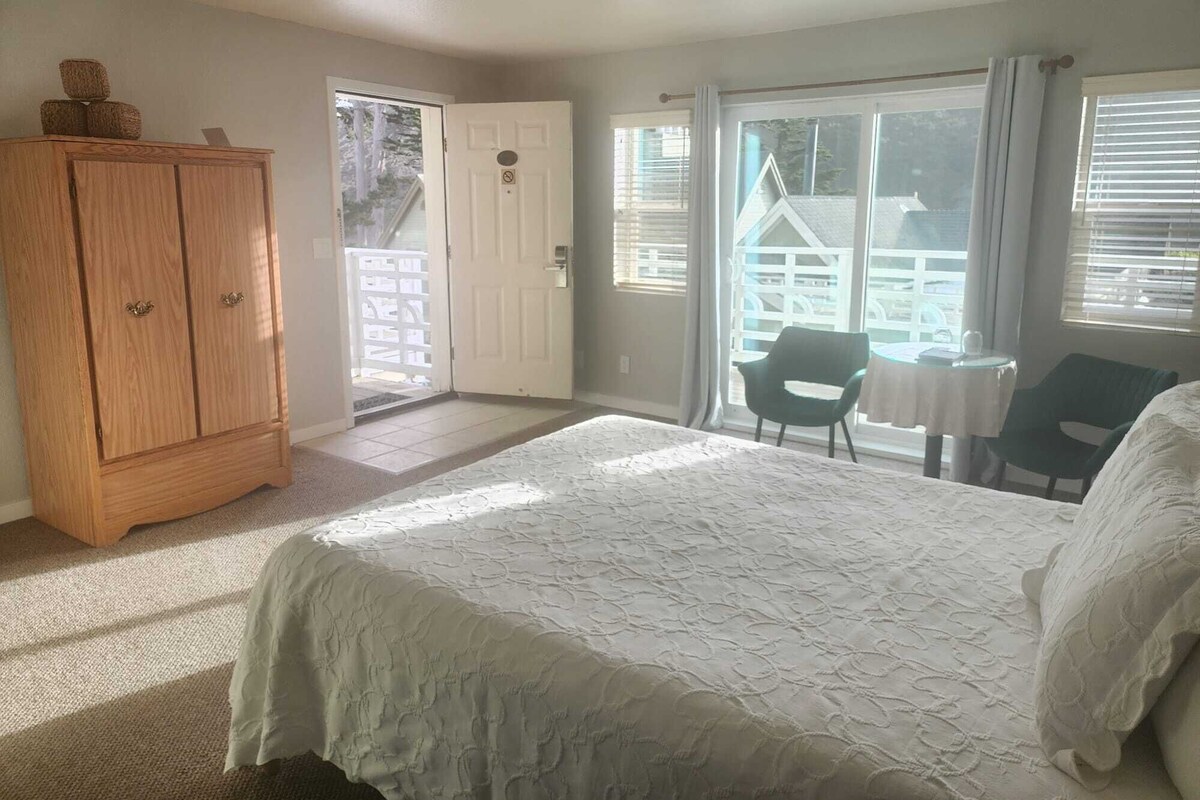 Een slaapkamer met een bed, een houten garderobe, een balkon met een tafel en stoelen en uitzicht op een huis.