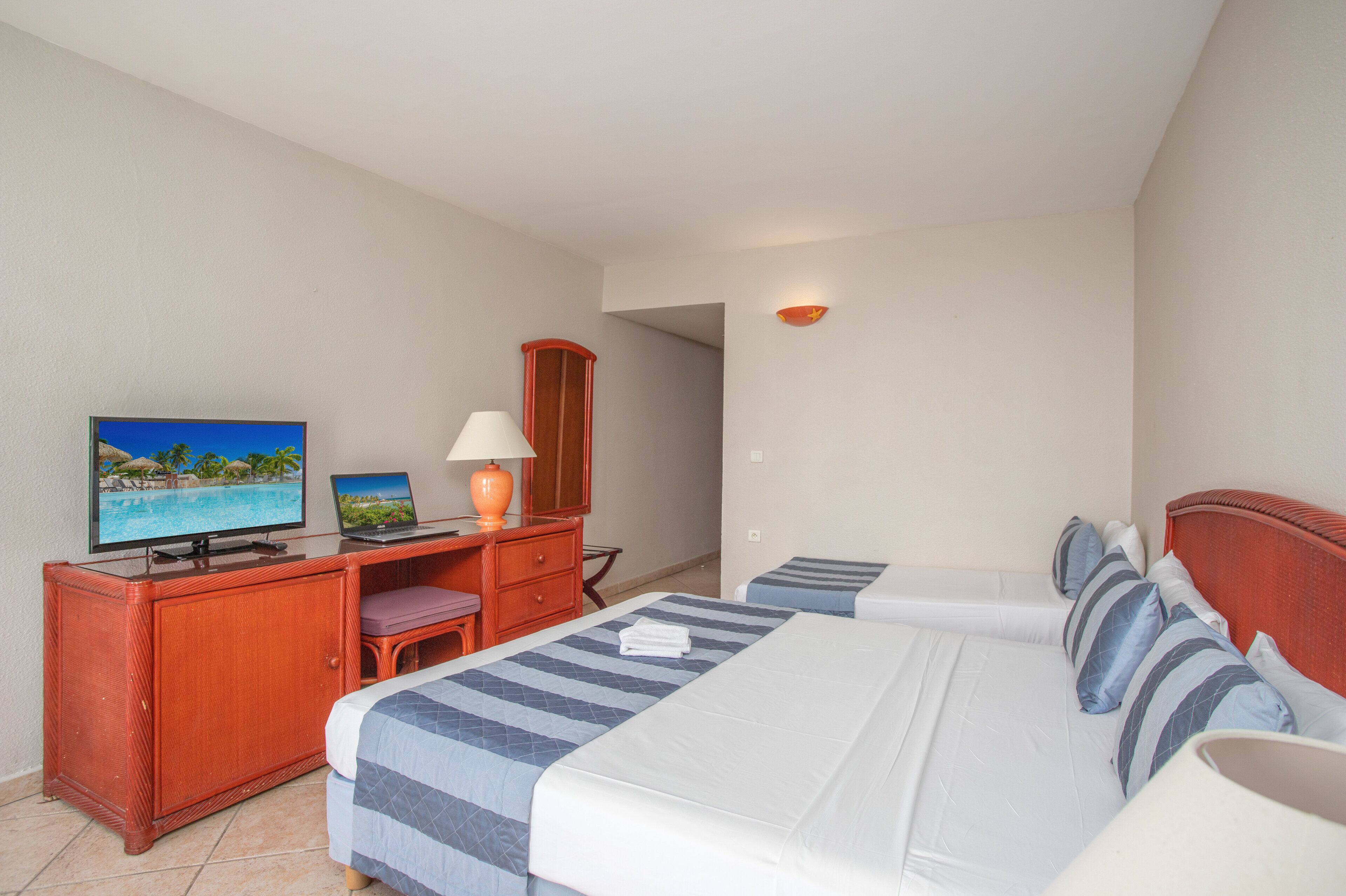 A hotel room with a bed, a desk with a TV, a lamp, and a wardrobe.