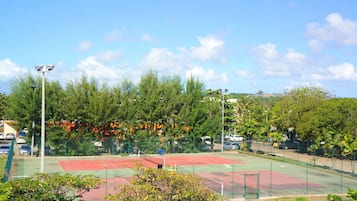 A tennis court surrounded by trees and a parking area.